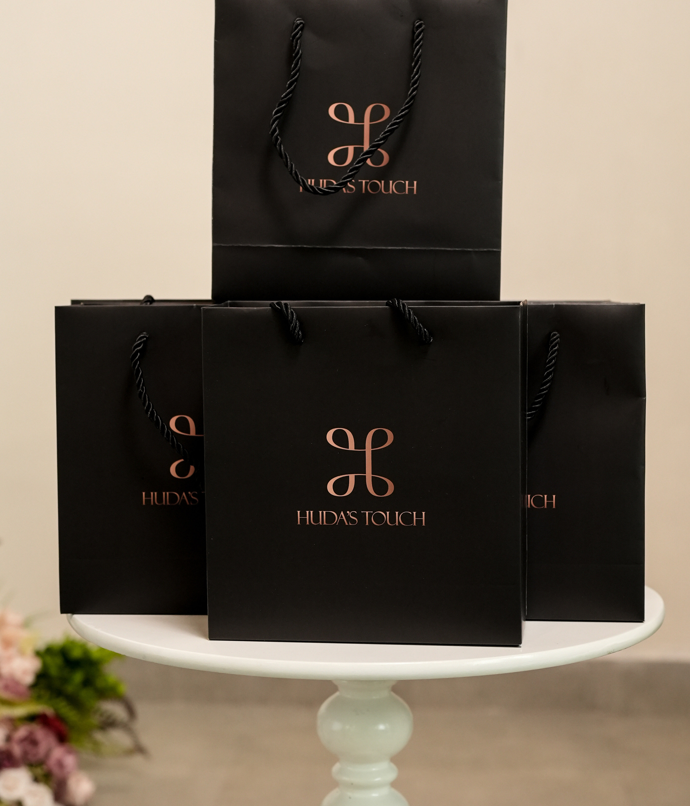 Black Huda's Touch paper bags with rose-gold foil logo